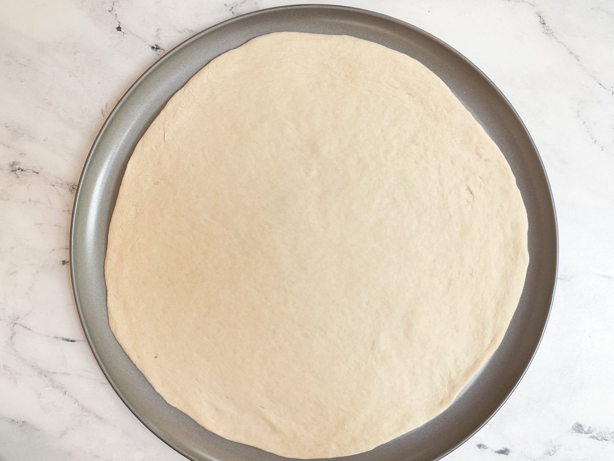 Unbaked pizza dough on pizza baking sheet.
