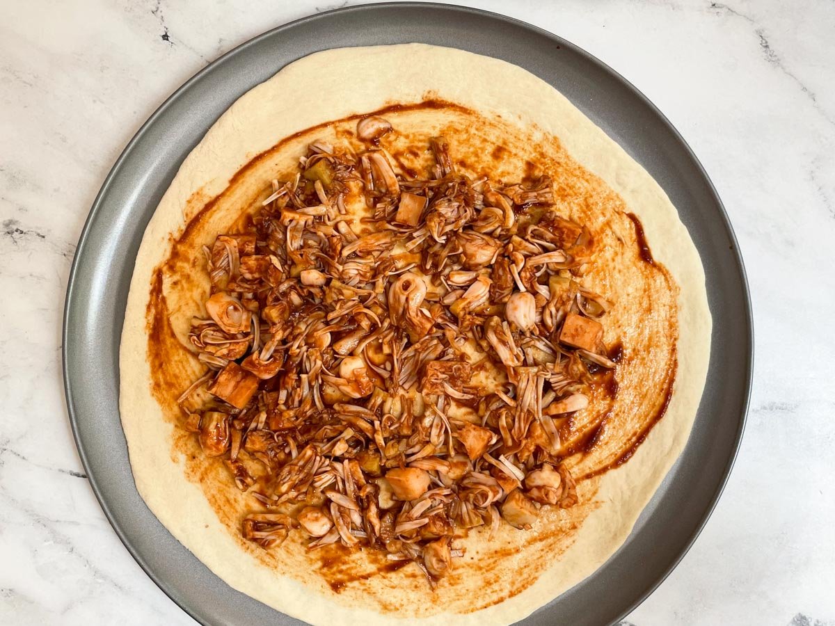 Unbaked pizza dough topped with BBQ sauce and jackfruit. 
