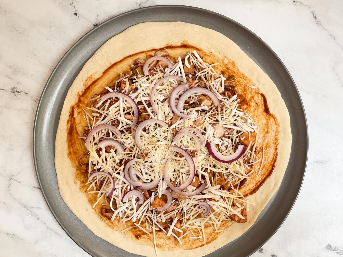 Unbaked BBQ jackfruit pizza topped with cheese and sliced onions. 