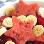 Close up of watermelon star served with sliced bananas, strawberries, and blueberries.