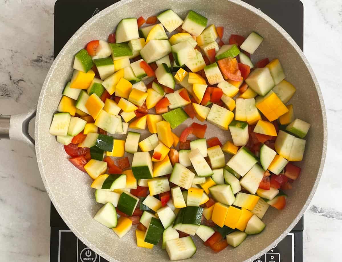 Diced red pepper, zucchini, yellow squash, and zucchini in sauté pan. 

