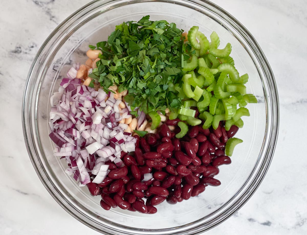 Chopped celery, chopped celery, and diced red onions, added to bowl of beans.
