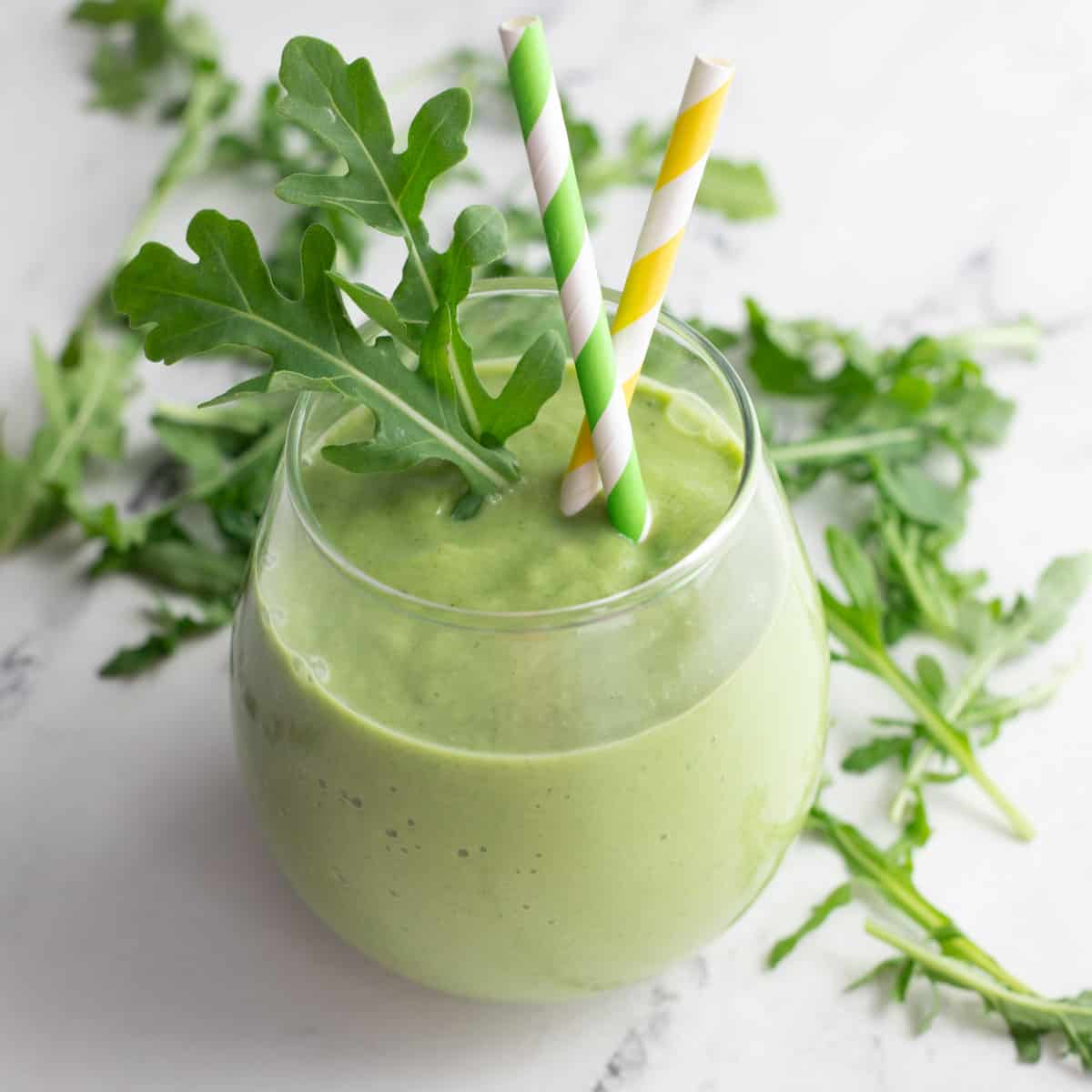 Arugula smoothie in glass with two straws. 