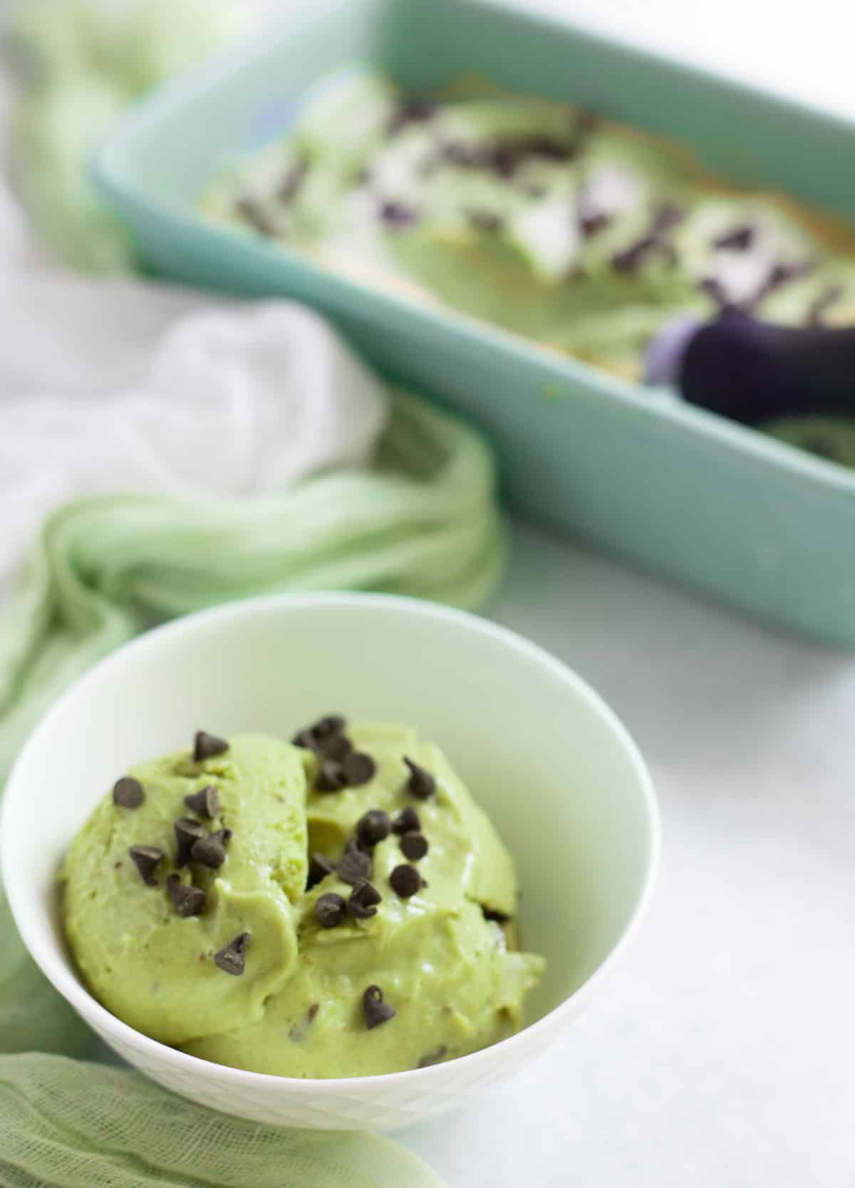 Green mint and avocado nice cream in white bowl topped with mini chocolate chips.

