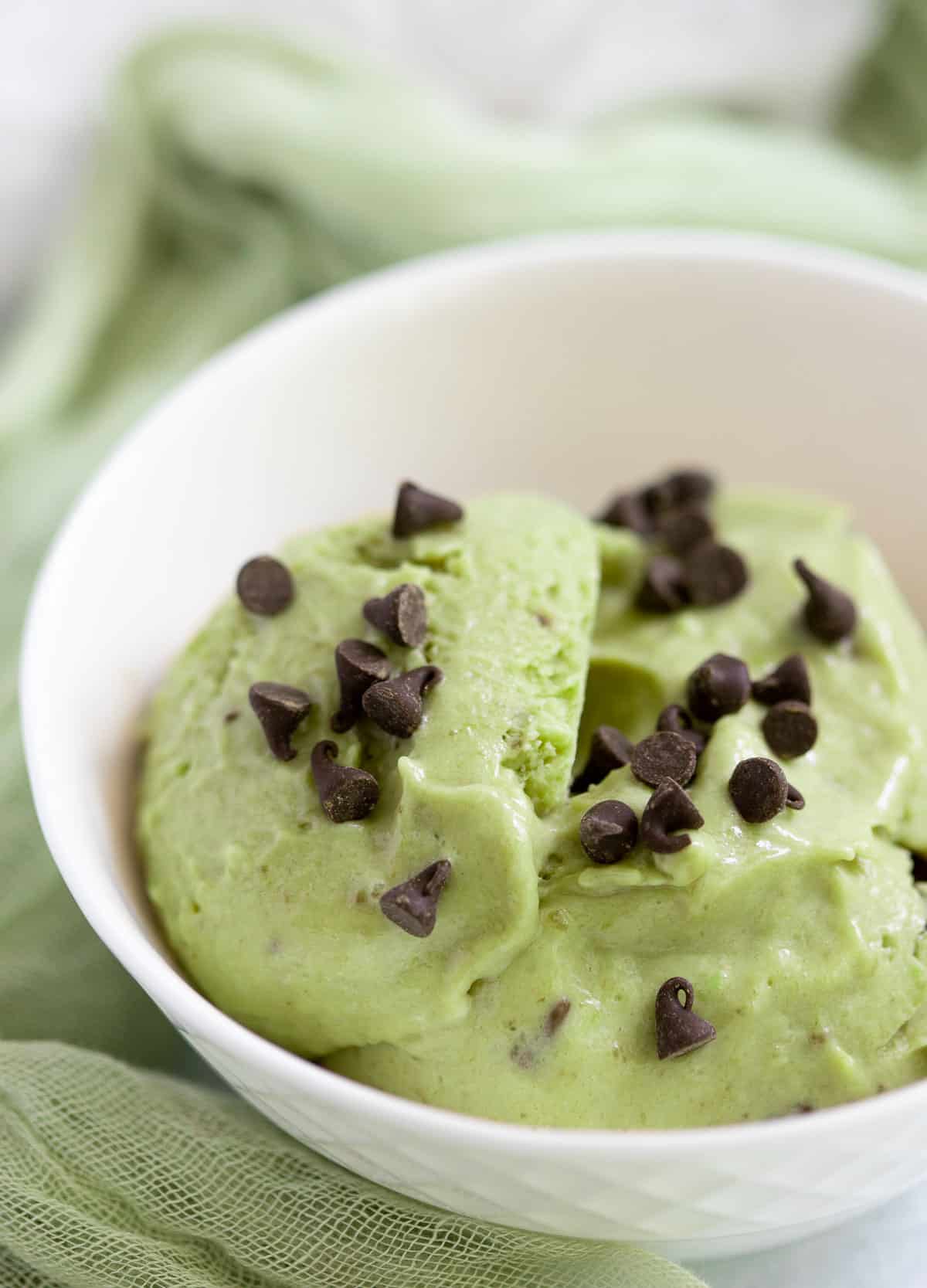 Avocado nice cream in white bowl topped with mini chocolate chips.
