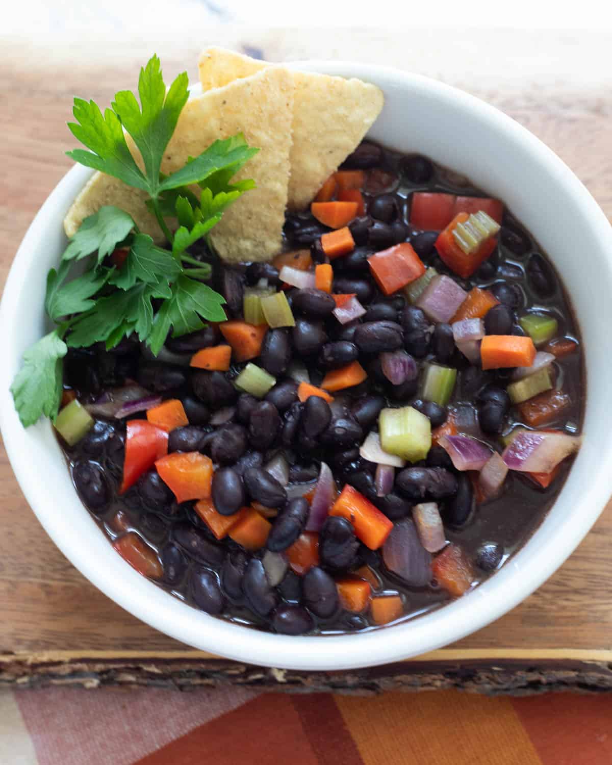Overhead of Copycat Panera black bean soup served with tortilla chips and fresh herbs.
