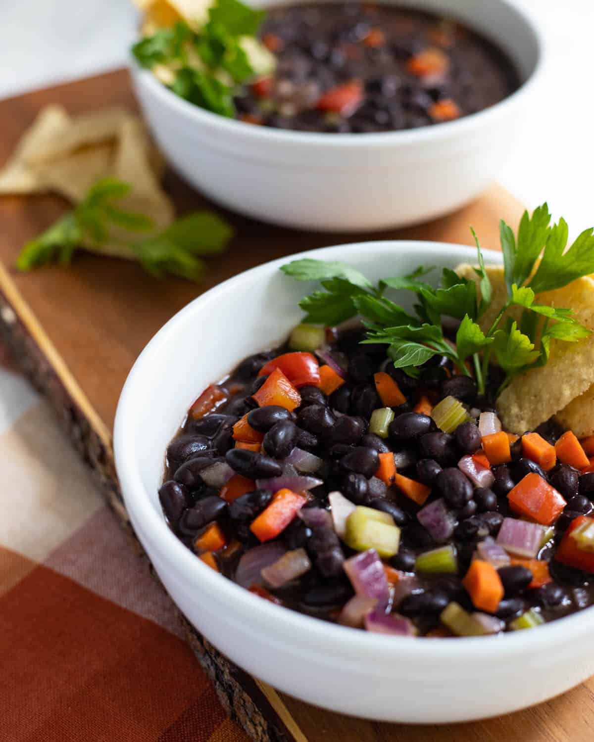 Black bean soup with red peppers and vegetables in white bowl.
