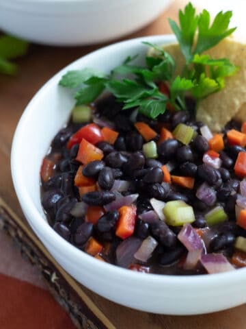 Black bean soup in white bowl with chips and parsley.