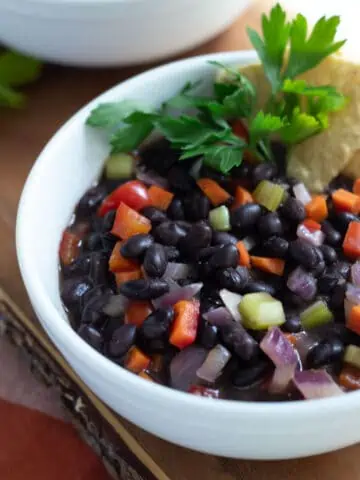Black bean soup in white bowl with chips and parsley.