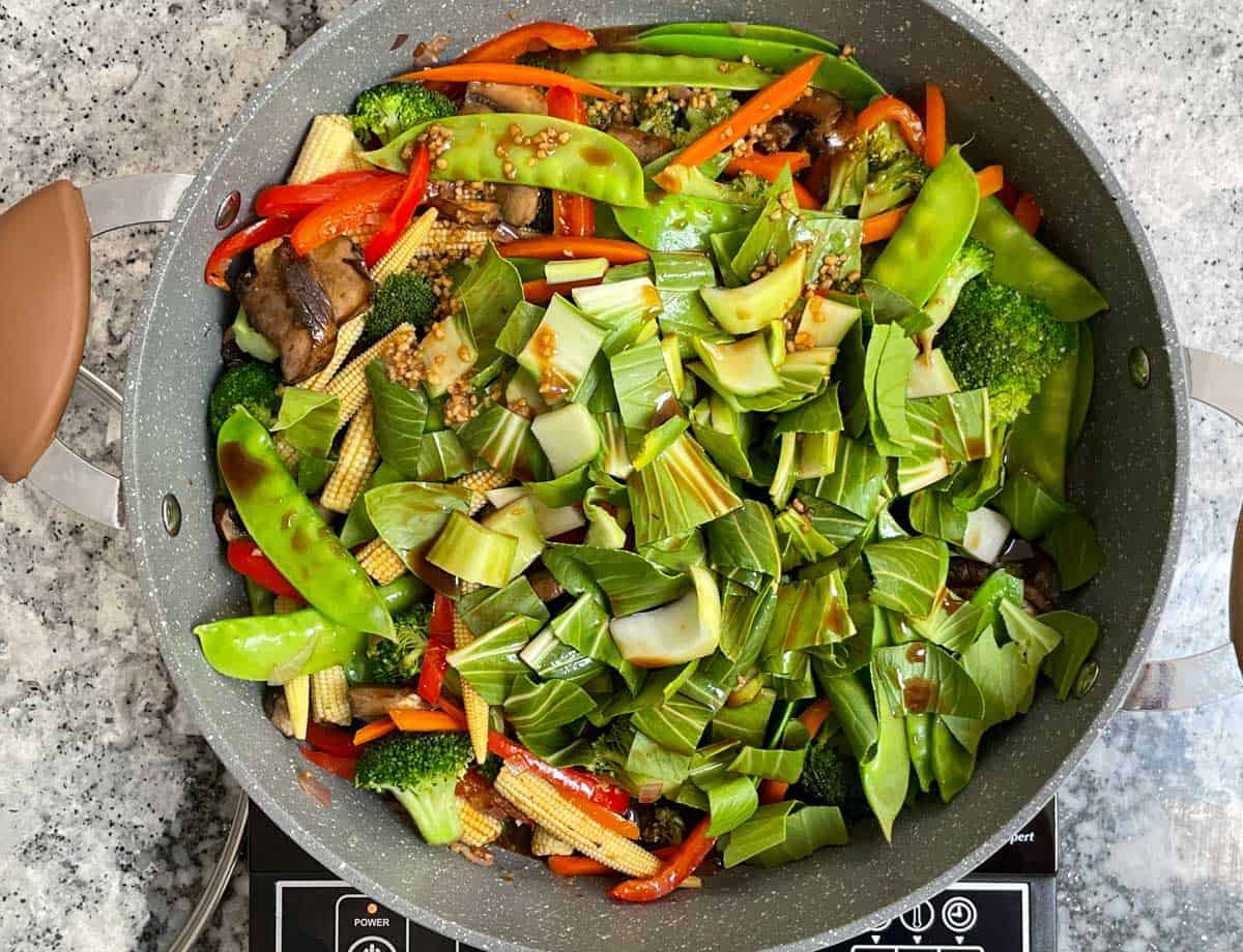 Bok choy and sauce added to saute pan filled with vegetables. 
