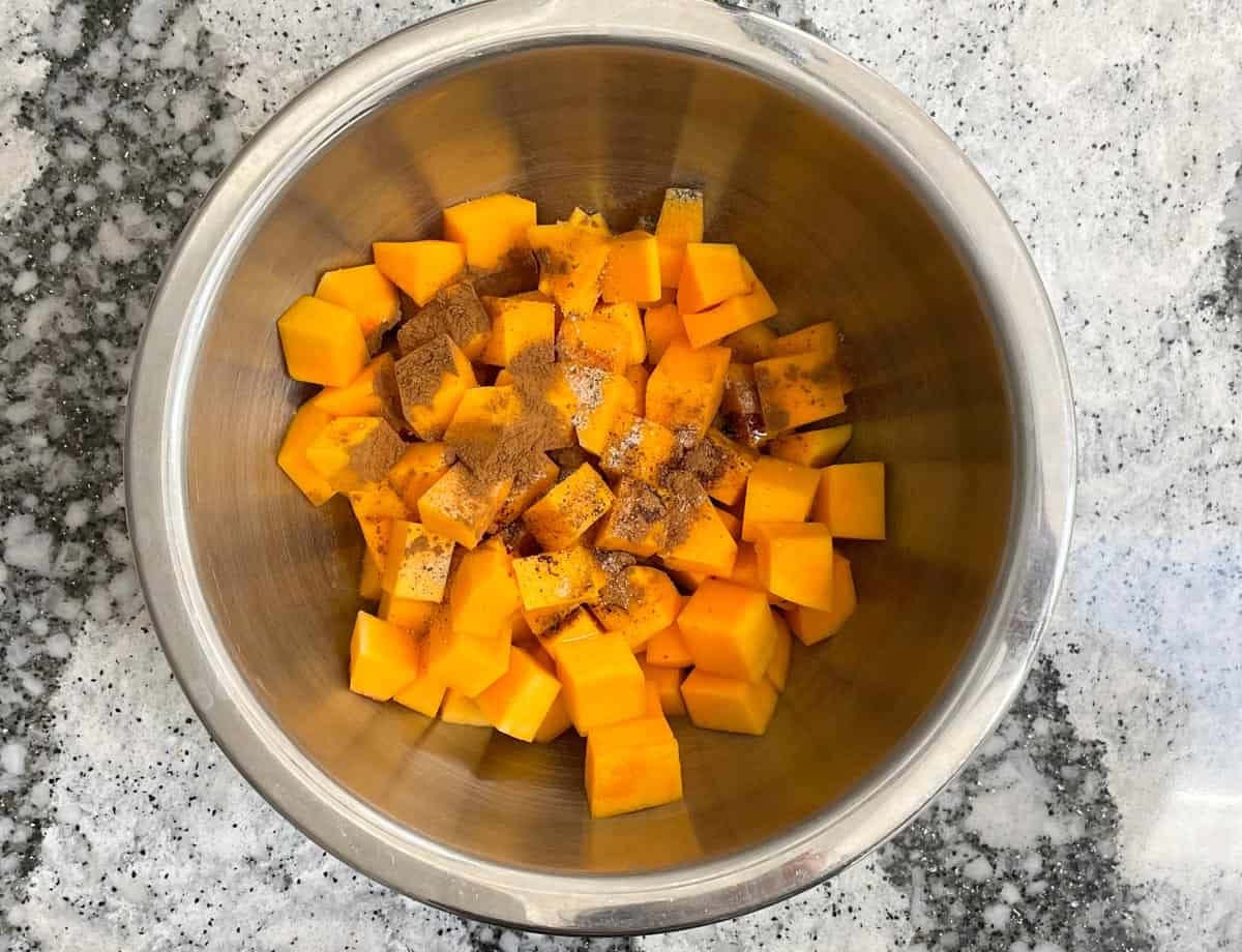Diced butternut squash topped with spices in a mixing bowl.
