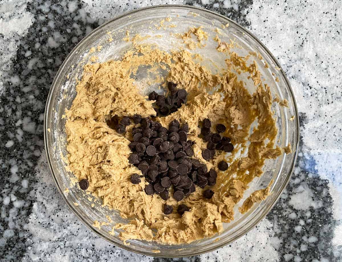 Adding chocolate chips to cookie batter in mixing bowl.
