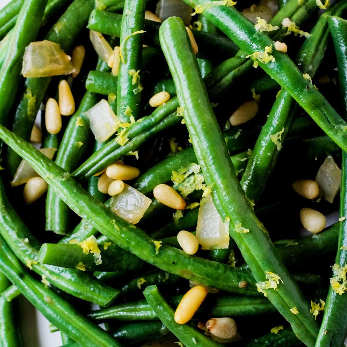 Close up of green beans topped with diced onions, pine nuts, and lemon zest.
