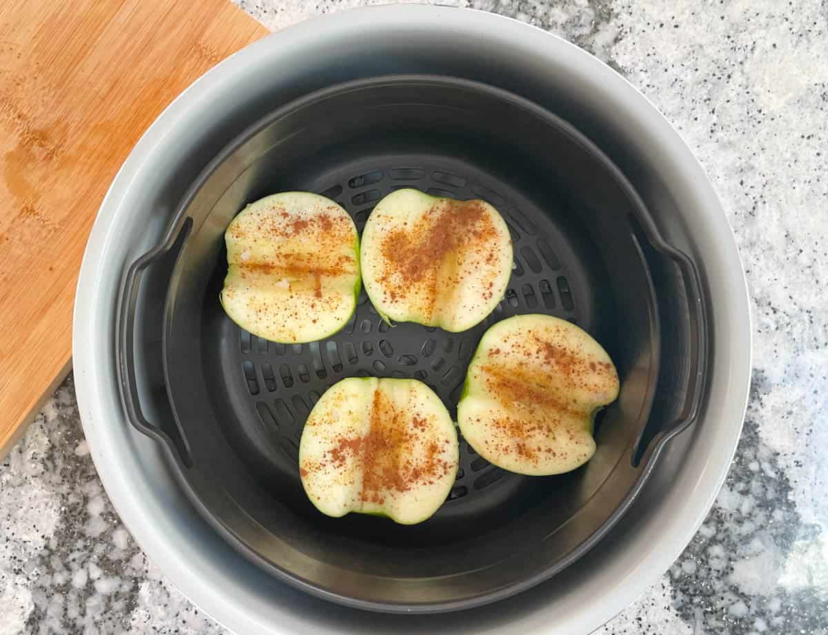 Apple halves topped with cinnamon in an air fryer basket.
