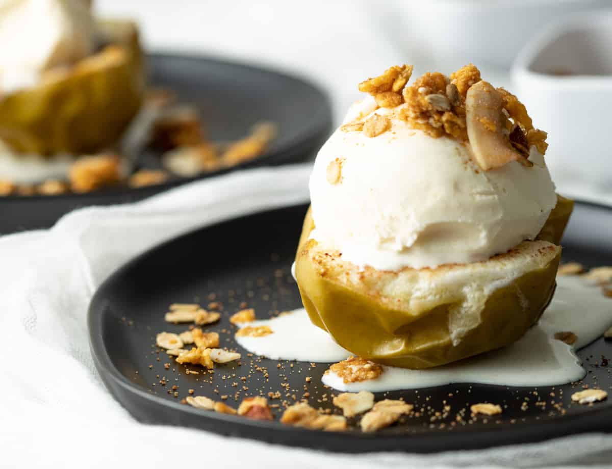 Vegan Baked apples served with a scoop of vanilla ice cream and topped with granola.
