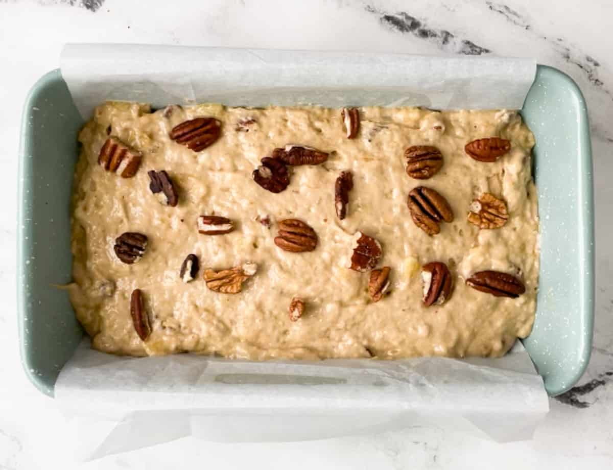 Banana bread batter in loaf pan topped with chopped nuts. 