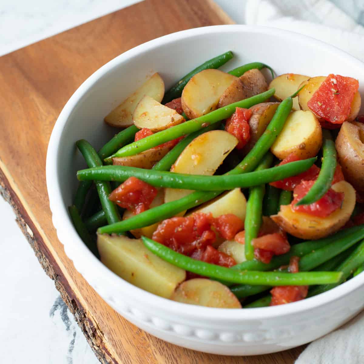 Potatoes and green beans in white serving bowl served with stewed tomatoes.
