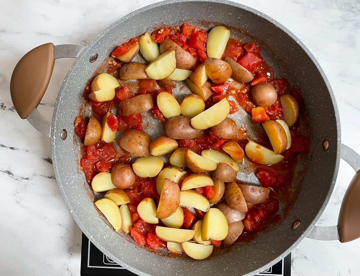 Potatoes added to diced tomatoes in pot. 