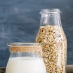 Glass of oat milk beside jug of oats.