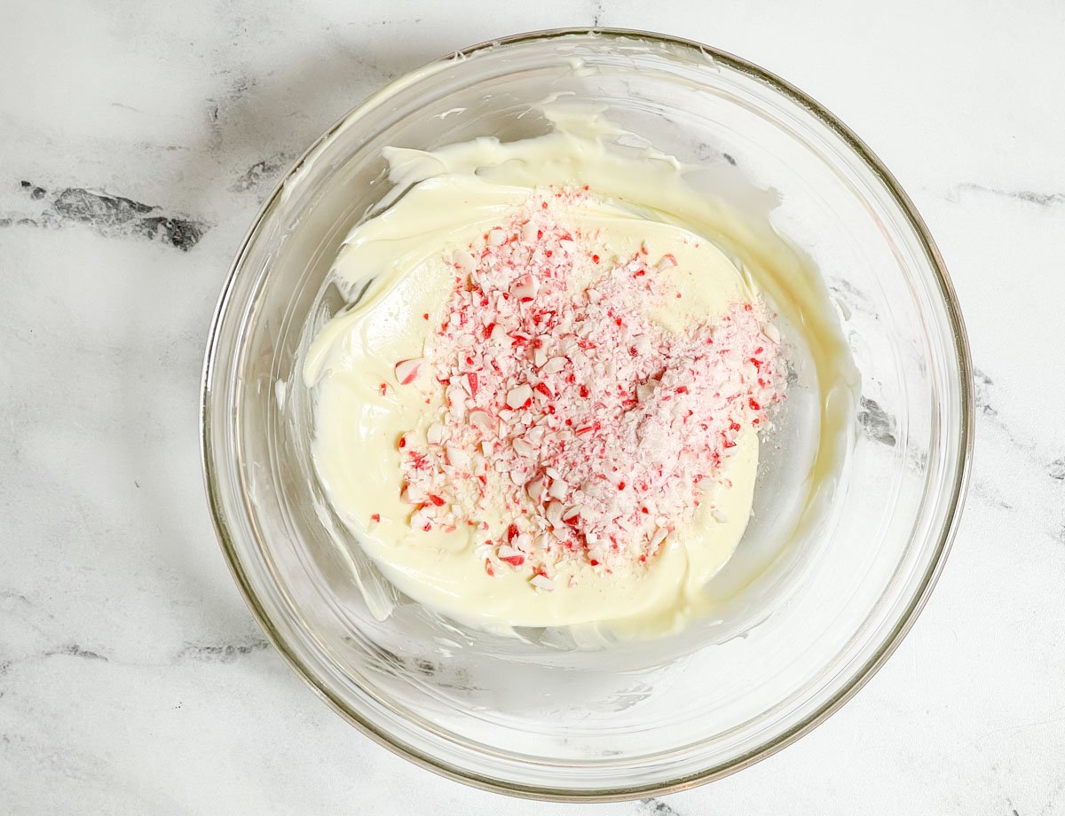 Candy cane pieces added to melted white chocolate in mixing bowl.
