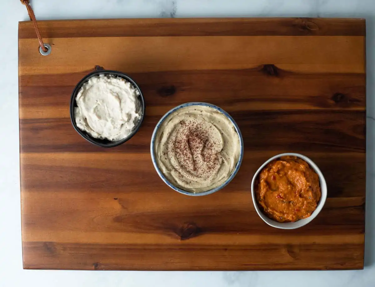 Vegan cheese spread, hummus, and eggplant spread on wood board. 
