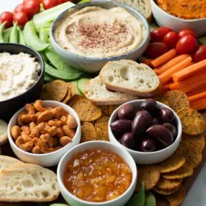 Vegan charcuterie board filled with dips, crackers, olives, and veggies.