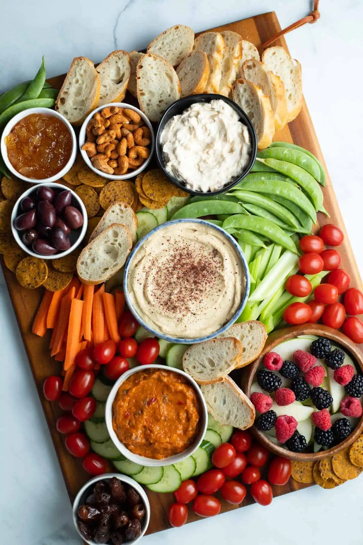 Vegan charcuterie board with hummus, vegan cheese spread, eggplant, sliced apples, berries, vegetables, olives, nuts, dates, jam. 