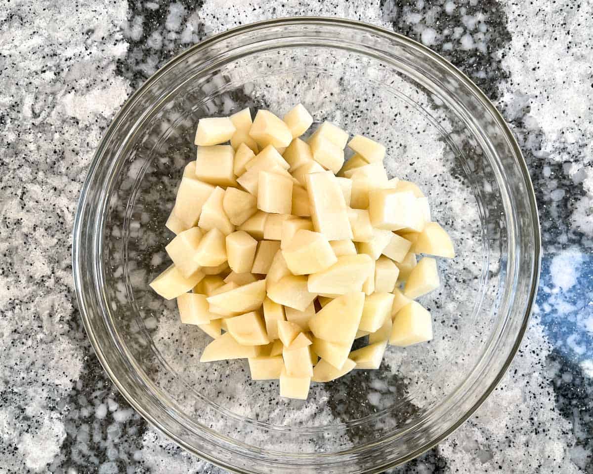 Diced and peeled potatoes in glass mixing bowl.
