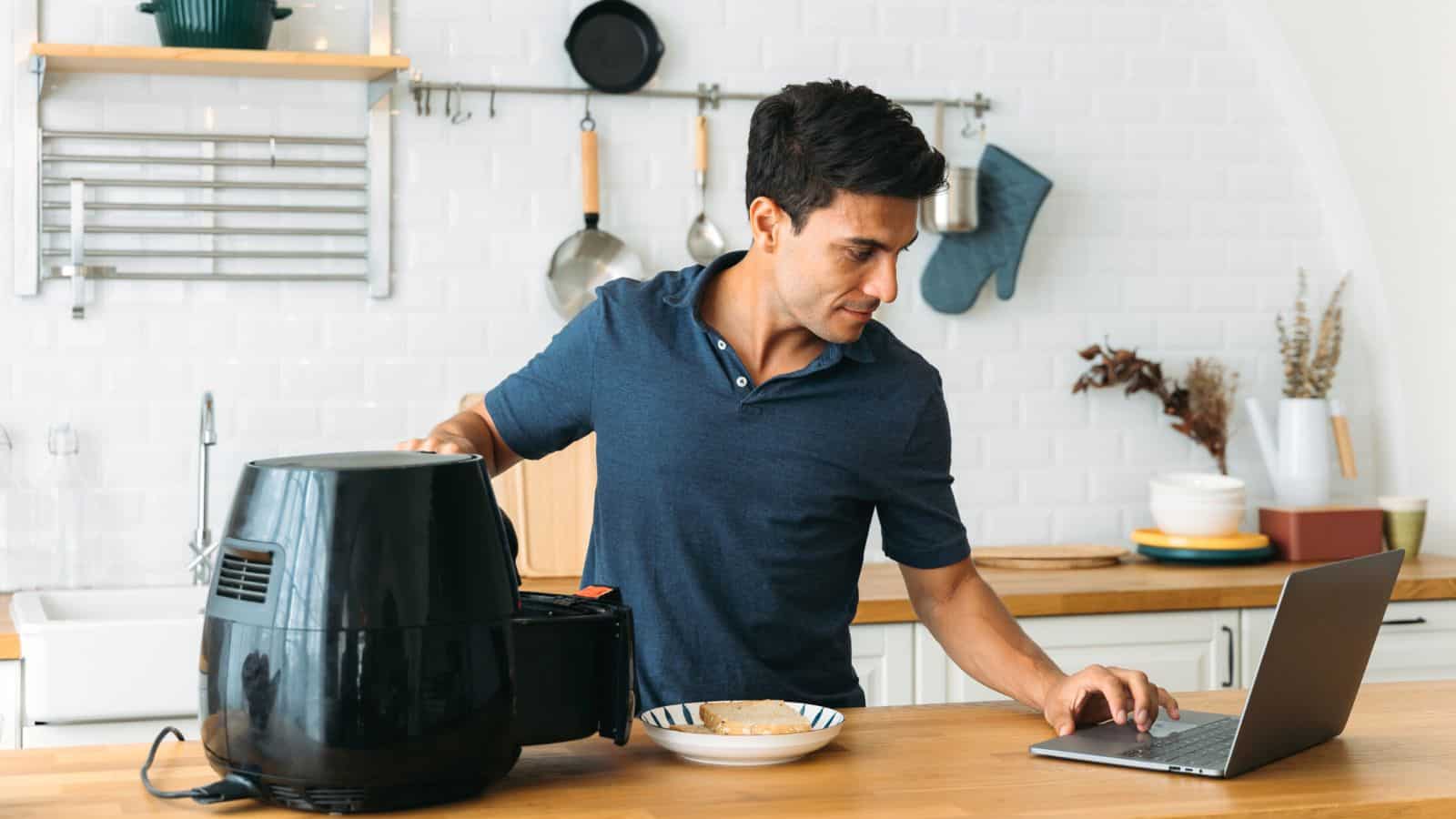 Man checking recipe on computer while working air fryer.
