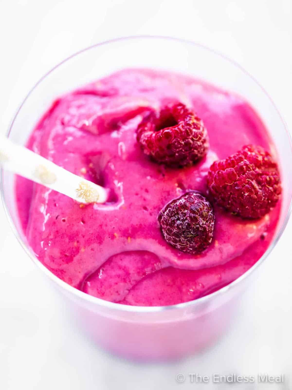 Berry smoothie in glass topped with frozen raspberries.
