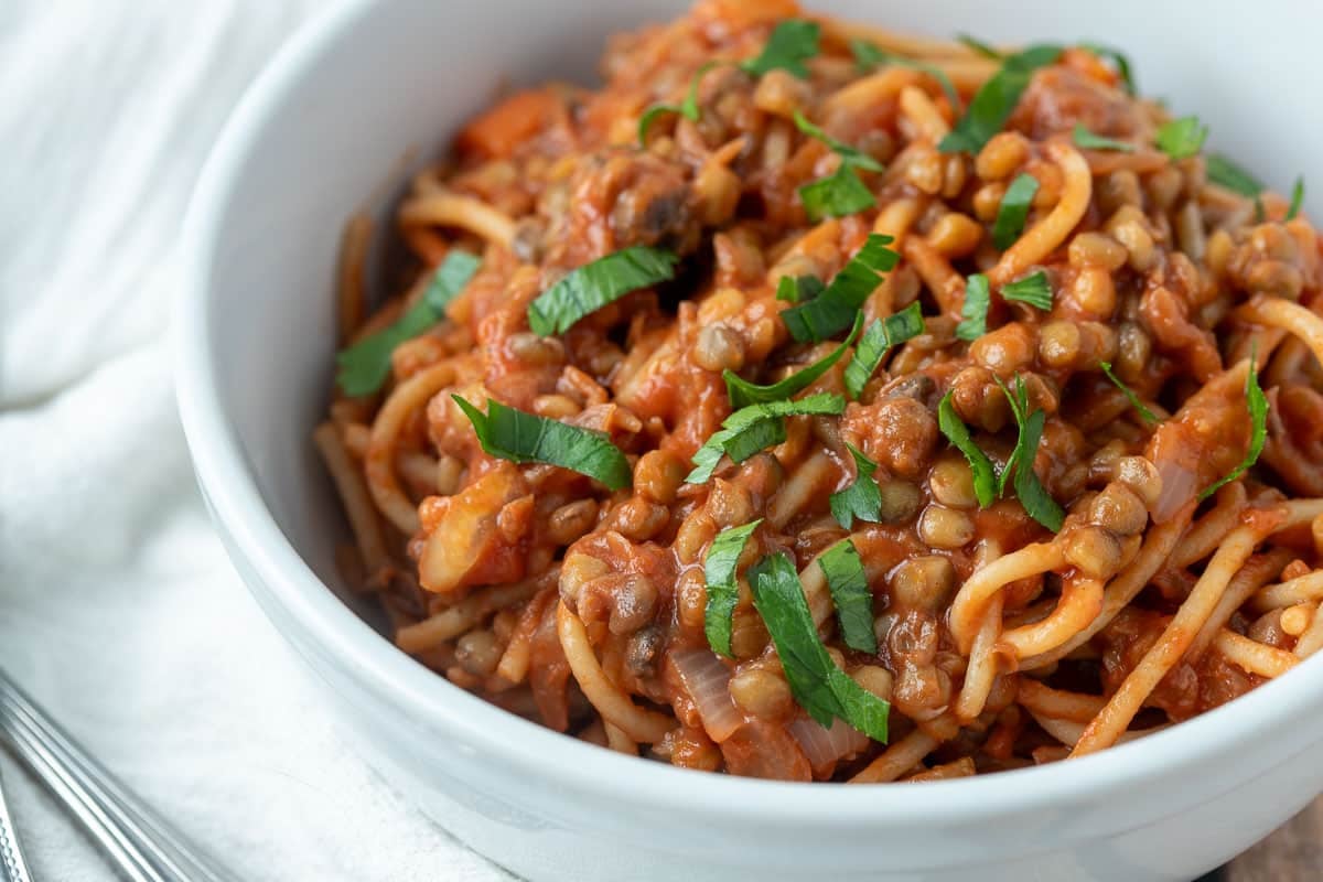 Whole wheat spaghetti and lentil bolognese in white bowl.