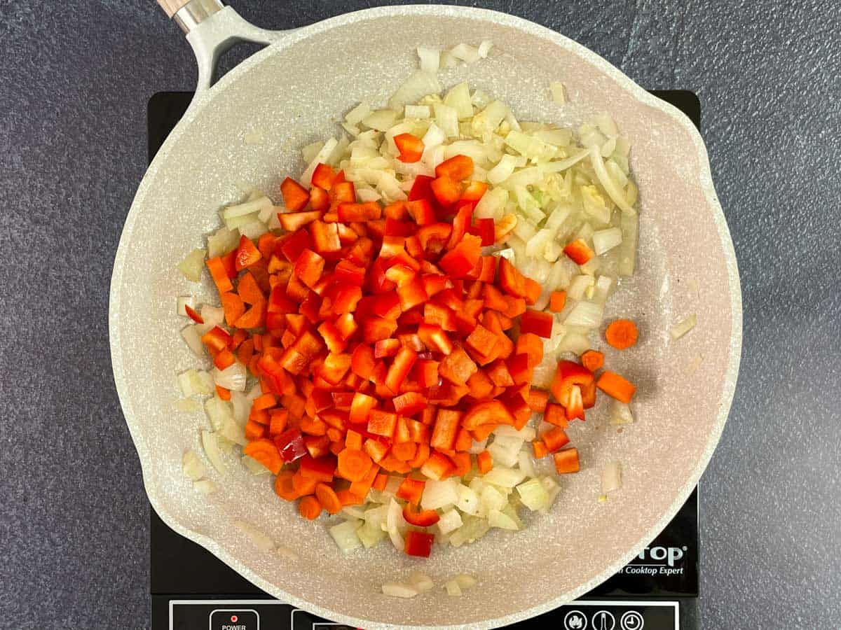 Adding carrots, and red peppers, to sauted onions in pan.