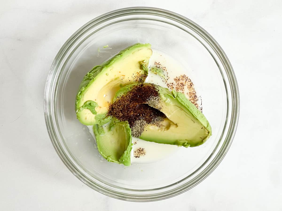 Avocado, spices, and almond milk in glass bowl.
