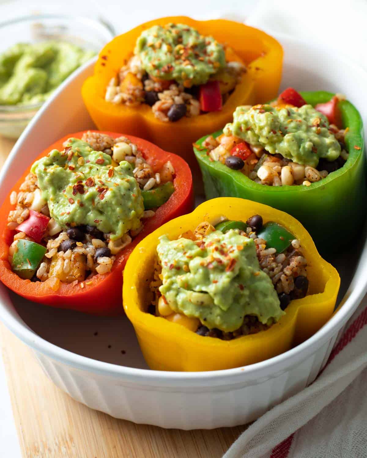 Vegan stuffed peppers topped with avocado cream in baking dish.

