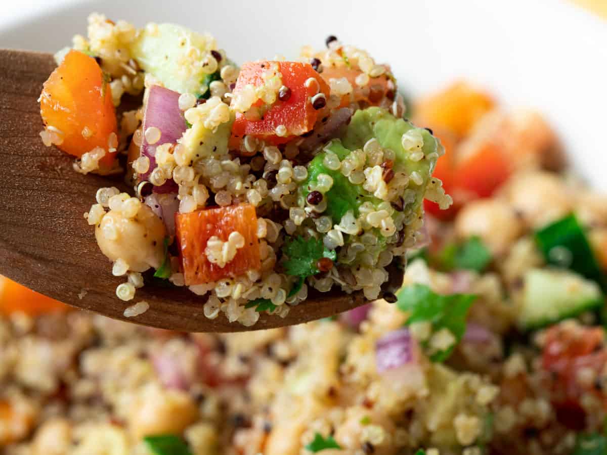 Spoon holding up a serving of quinoa and vegetable salad.
