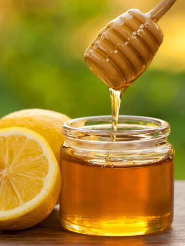 Honey wand dipped in a jar of honey beside a lemon cut in half.