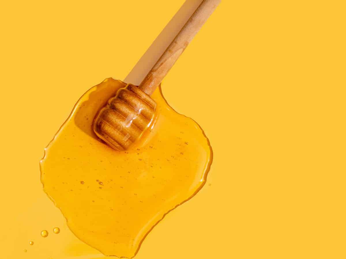 Honey wand with sticky honey puddle on yellow background.
