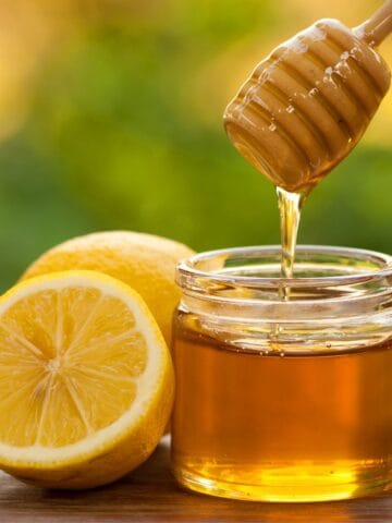Honey wand dipped in a jar of honey beside a lemon cut in half.