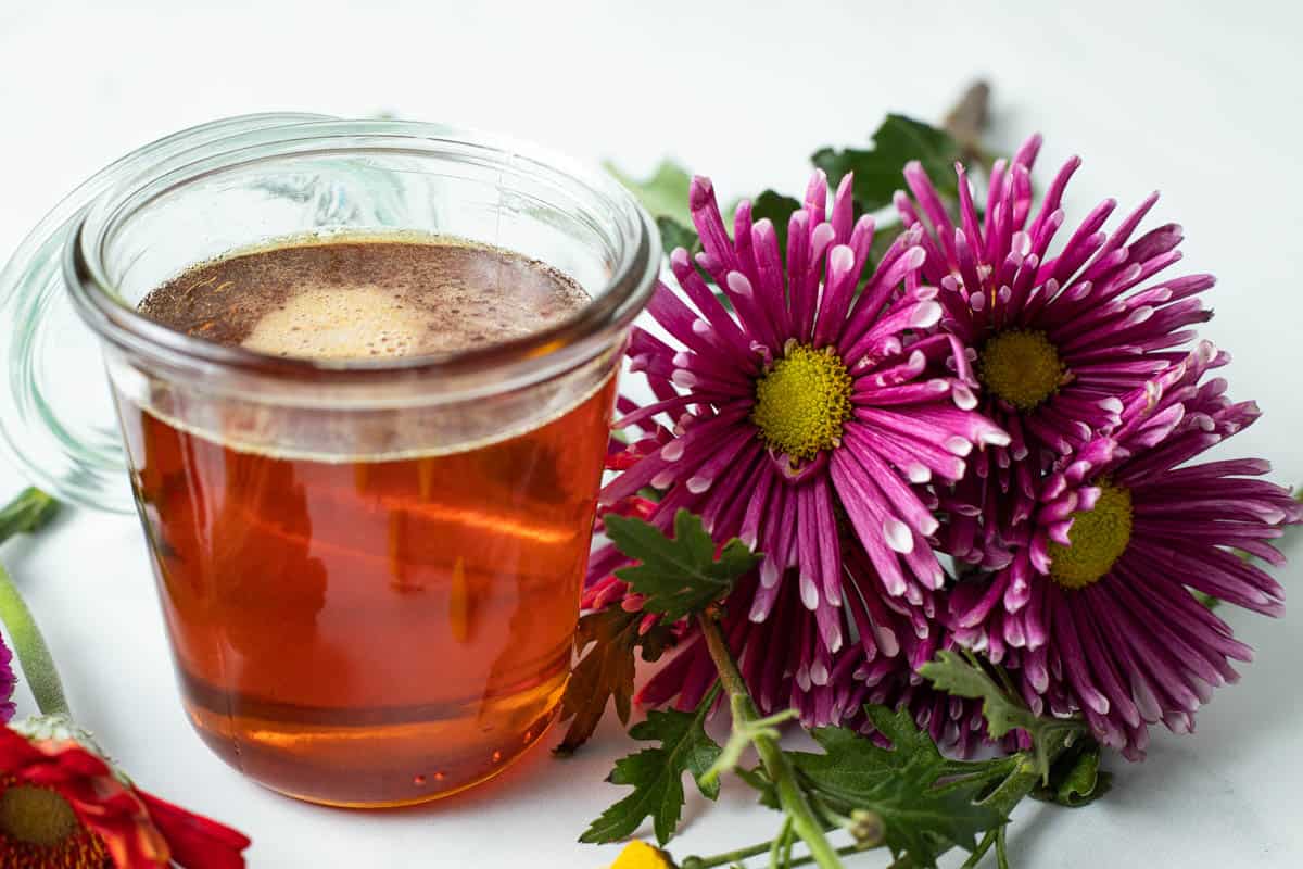 Vegan honey in jar beside colorful flowers.
