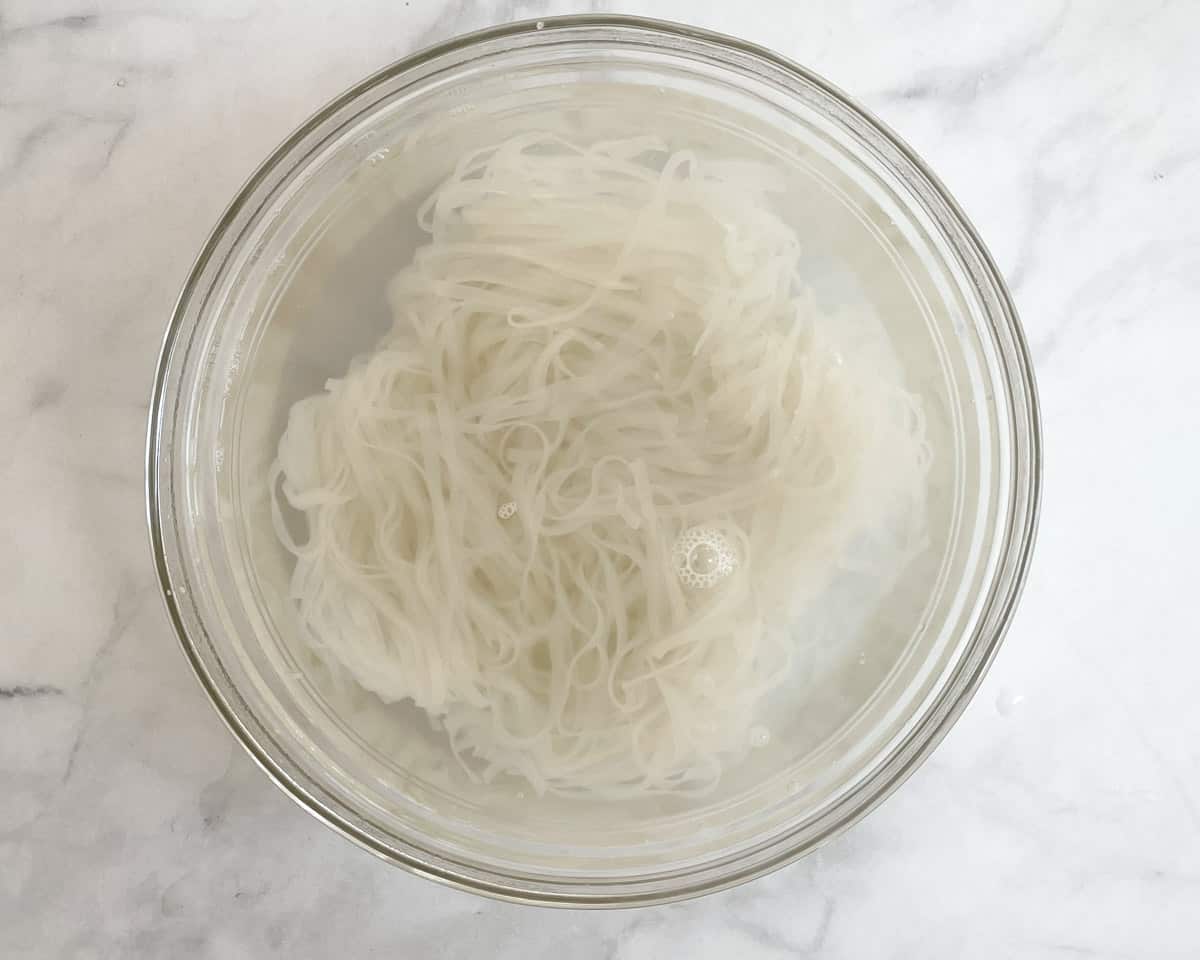 Rice noodles in large bowl covered with boiling water.
