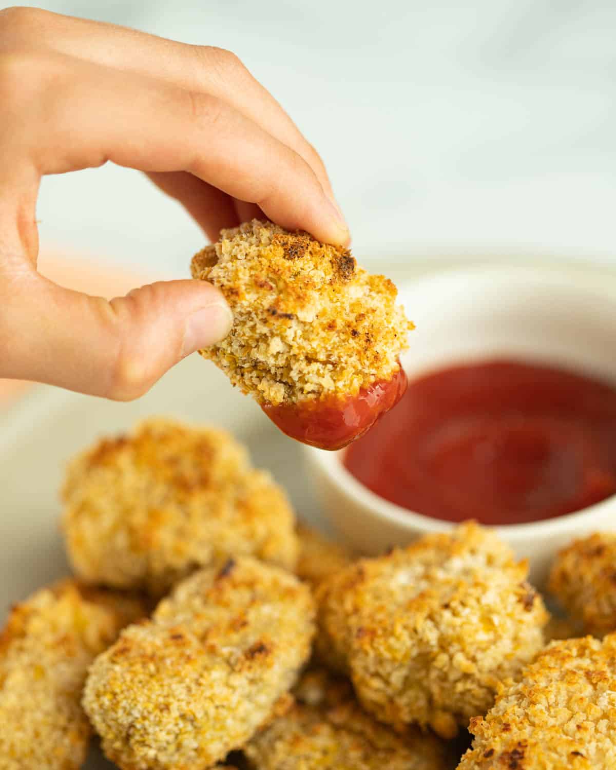 Hand dipping tofu chicken nuggets in ketchup.
