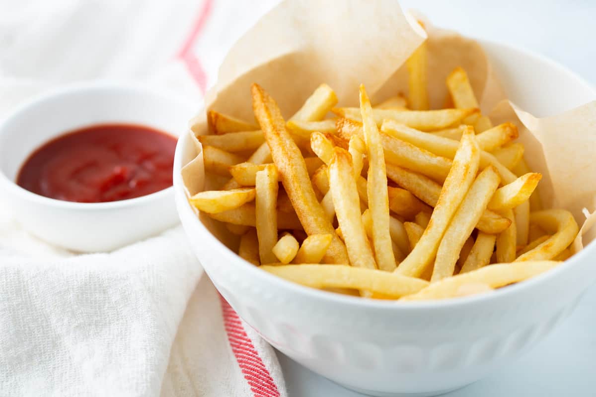 Shoestring fries in white bowl with a side of ketchup. 