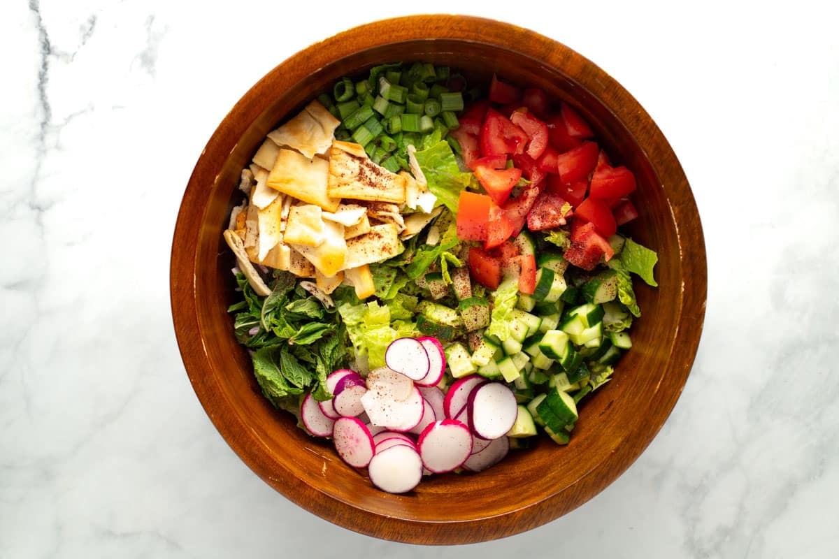 Fattoush salad ingredients in a wood bowl.
