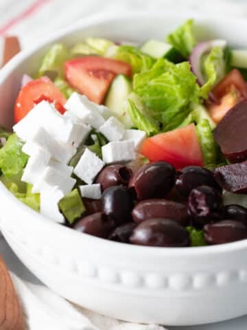 Vegan greek salad in a white bowl.