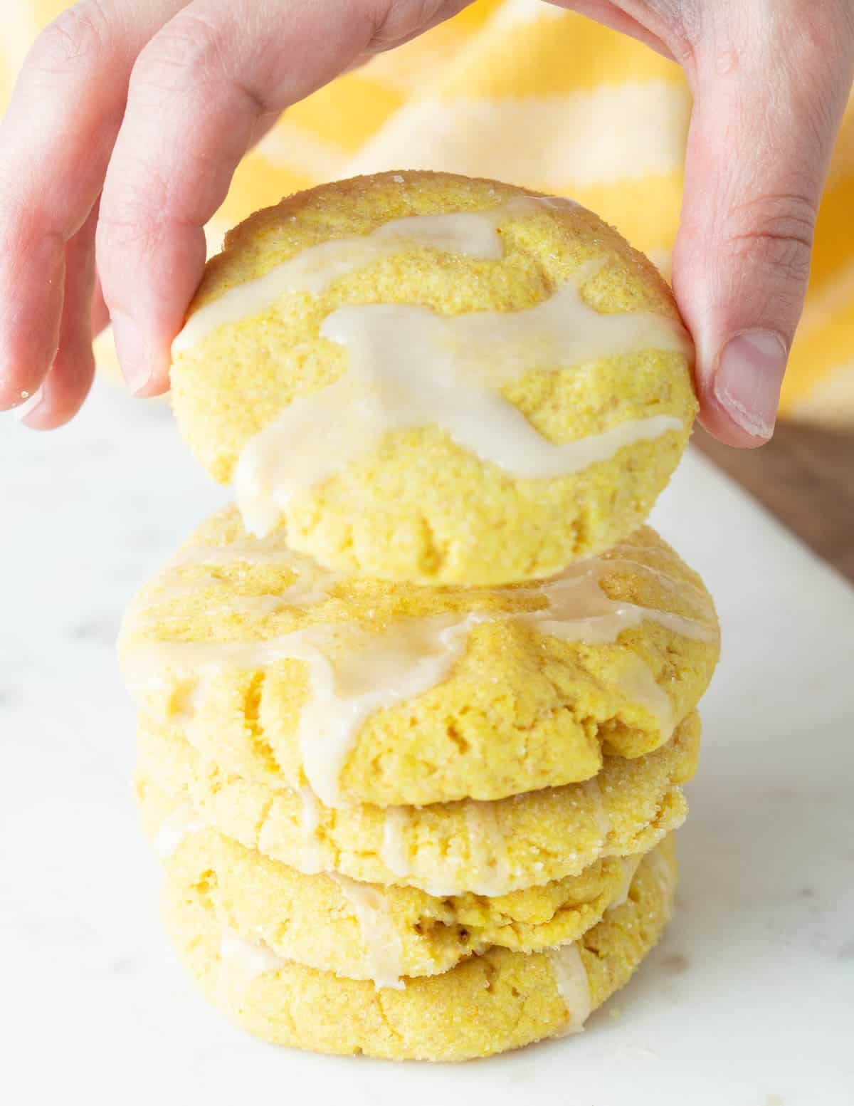 Hand lifting lemon cookie from a stack of lemon cookies. 
