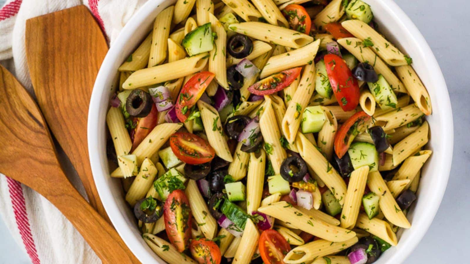 Pasta salad with fresh herbs, tomatoes, and black olives. 
