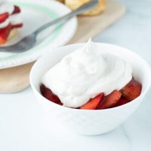Fresh strawberries in a bowl topped with vegan whipped cream.