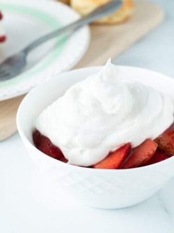 Fresh strawberries in a bowl topped with vegan whipped cream.