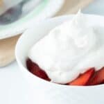 Bowl of strawberries topped with vegan whipped cream.