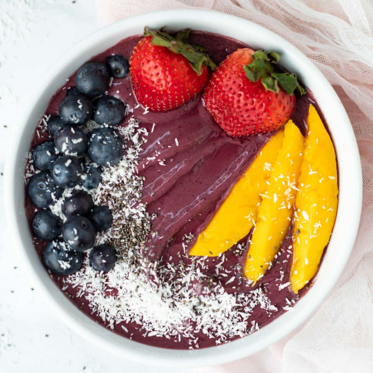 Acai bowl topped with fresh blueberries, strawberries, mango, coconut flakes, and chia seeds.